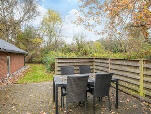 An outdoor patio with a brick floor, a wooden fence, and a table with chairs.