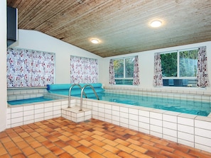 An indoor swimming pool with tiled flooring, a wooden ceiling, and patterned curtains.