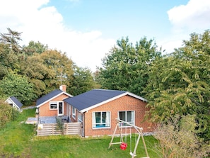 A two-story brick house with a dark roof, a swing set, and a small garden area.