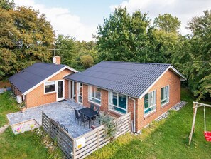 A two-story brick house with a patio, a wooden fence, and a swing set. - 4 Star Holiday Home in Glesborg (Glesborg)