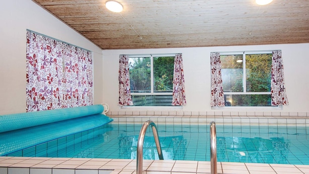 An indoor swimming pool with tiled walls, a wooden ceiling, and windows with floral curtains. - 4 Star Holiday Home in Glesborg (Glesborg)