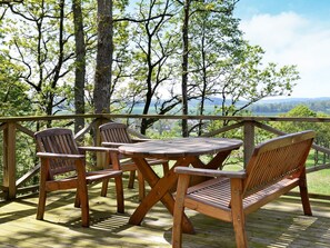 A wooden deck with a table and four chairs, overlooking a scenic landscape.