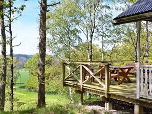 A wooden deck with outdoor seating, surrounded by trees and a view of a green landscape.