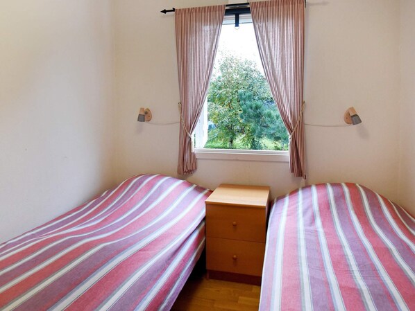 A small room with two single beds, a wooden nightstand, and a window with curtains.