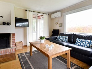 Una sala de estar con chimenea, una mesa de madera, un sofá de cuero negro y un ventanal grande.