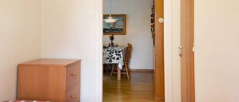 A room with two beds, a wooden dresser, a dining table with a patterned tablecloth, and a painting on the wall.