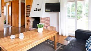 A living room with a fireplace, a television mounted on the wall, and a black leather sofa. - 5 Person Holiday Home in Glommen (Glommen)