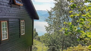 Une maison en bois sombre, offrant une vue sur un lac et des montagnes.