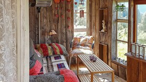 Une pièce chaleureuse avec un décor intérieur en bois, un canapé matelassé, une petite table et une fenêtre donnant sur des arbres.
