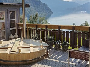 A wooden deck with a hot tub, a wooden fence, and a view of a lake and mountains. - 7 Person Holiday Home in Skjolden (Luster)