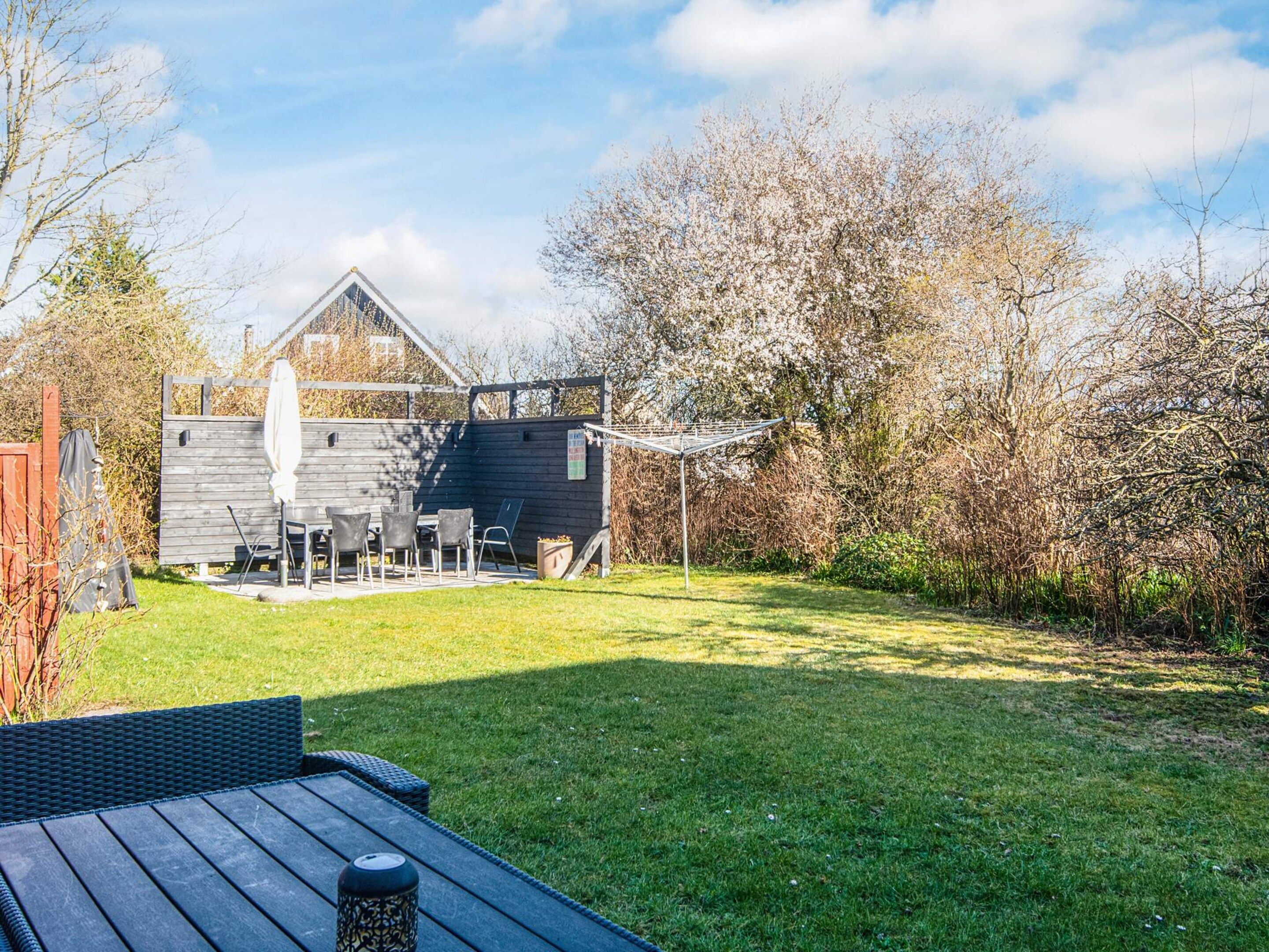 A backyard with a wooden deck, a grill, and a covered patio area.
