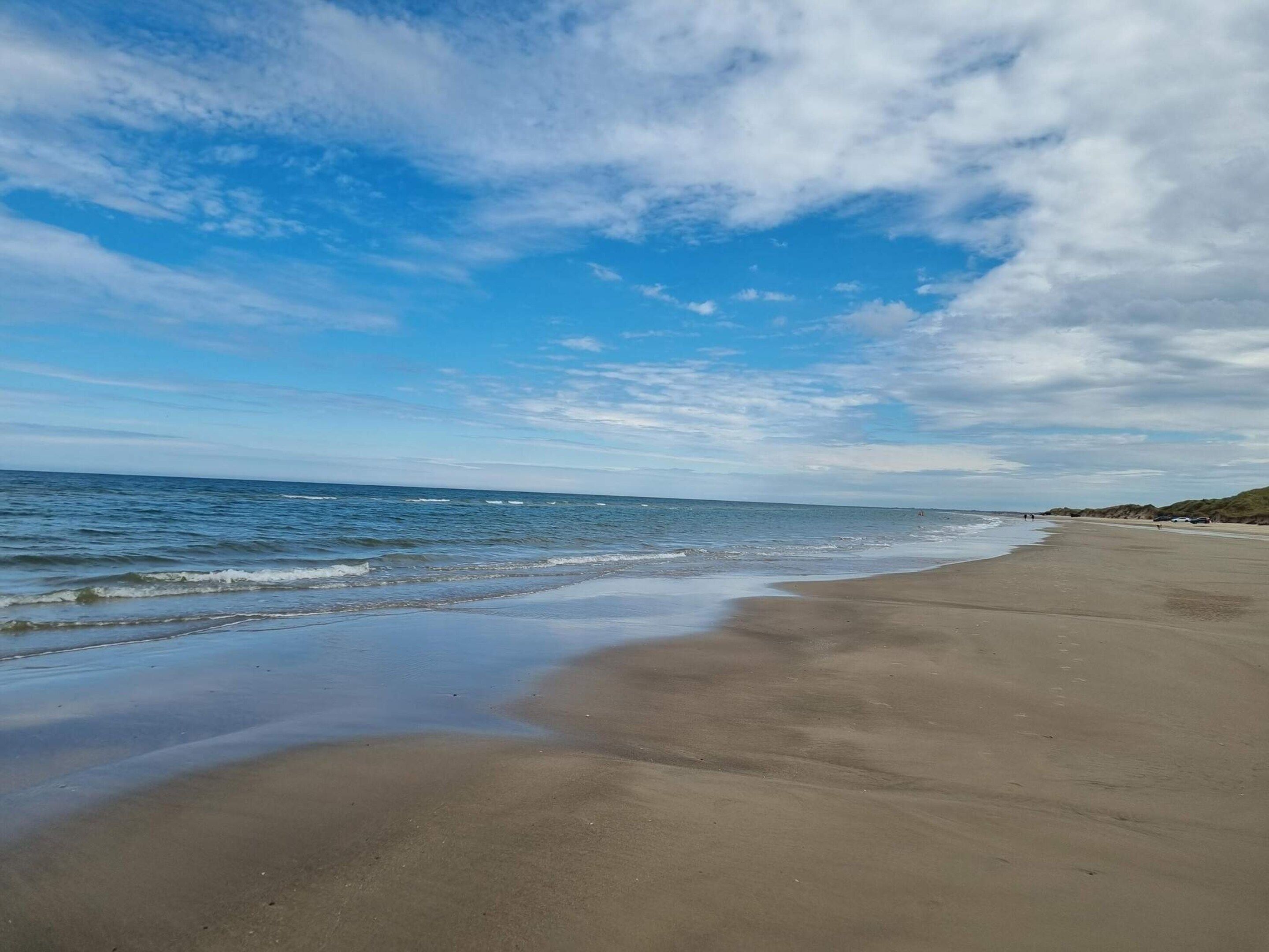 A beach with a wide sandy shore, gentle waves, and a partly cloudy sky.