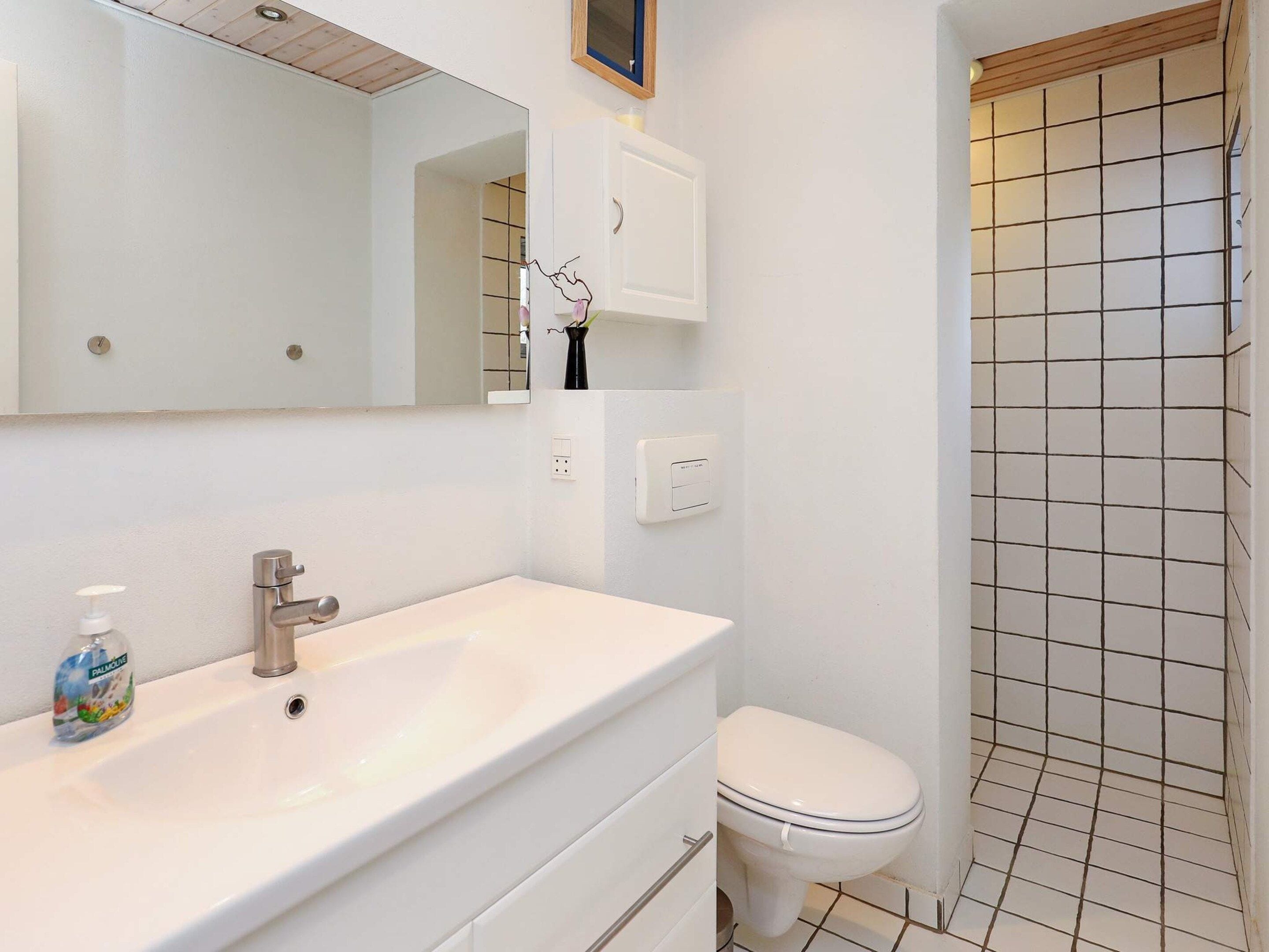 Een badkamer met een witte wastafel, een spiegel, een toilet en een douche.