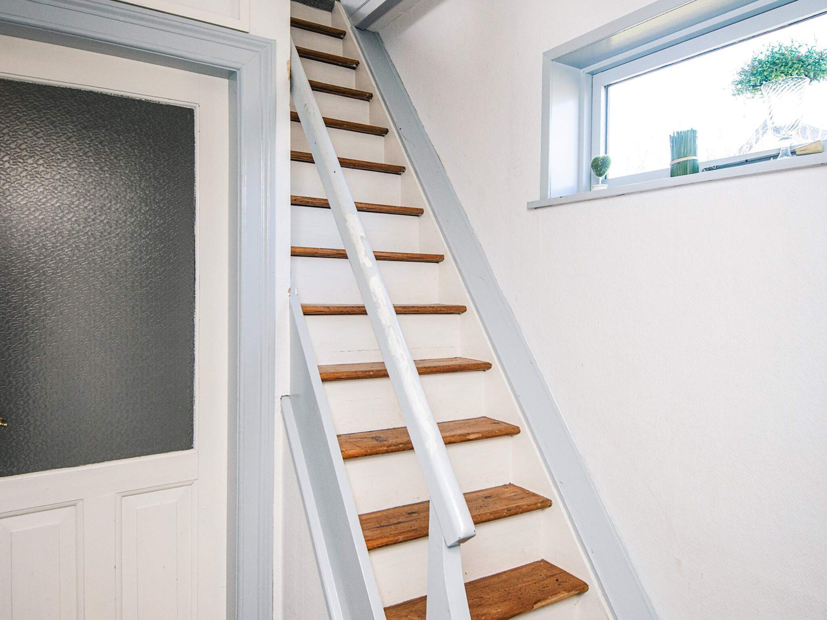 Eine Treppe mit Holzdielen und weißen Geländern, die zu einer Tür mit einer Türscheibe aus strukturiertem Glas führt.