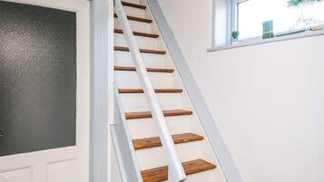 Eine Treppe mit Holzdielen und weißen Geländern, die zu einer Tür mit einer Türscheibe aus strukturiertem Glas führt.