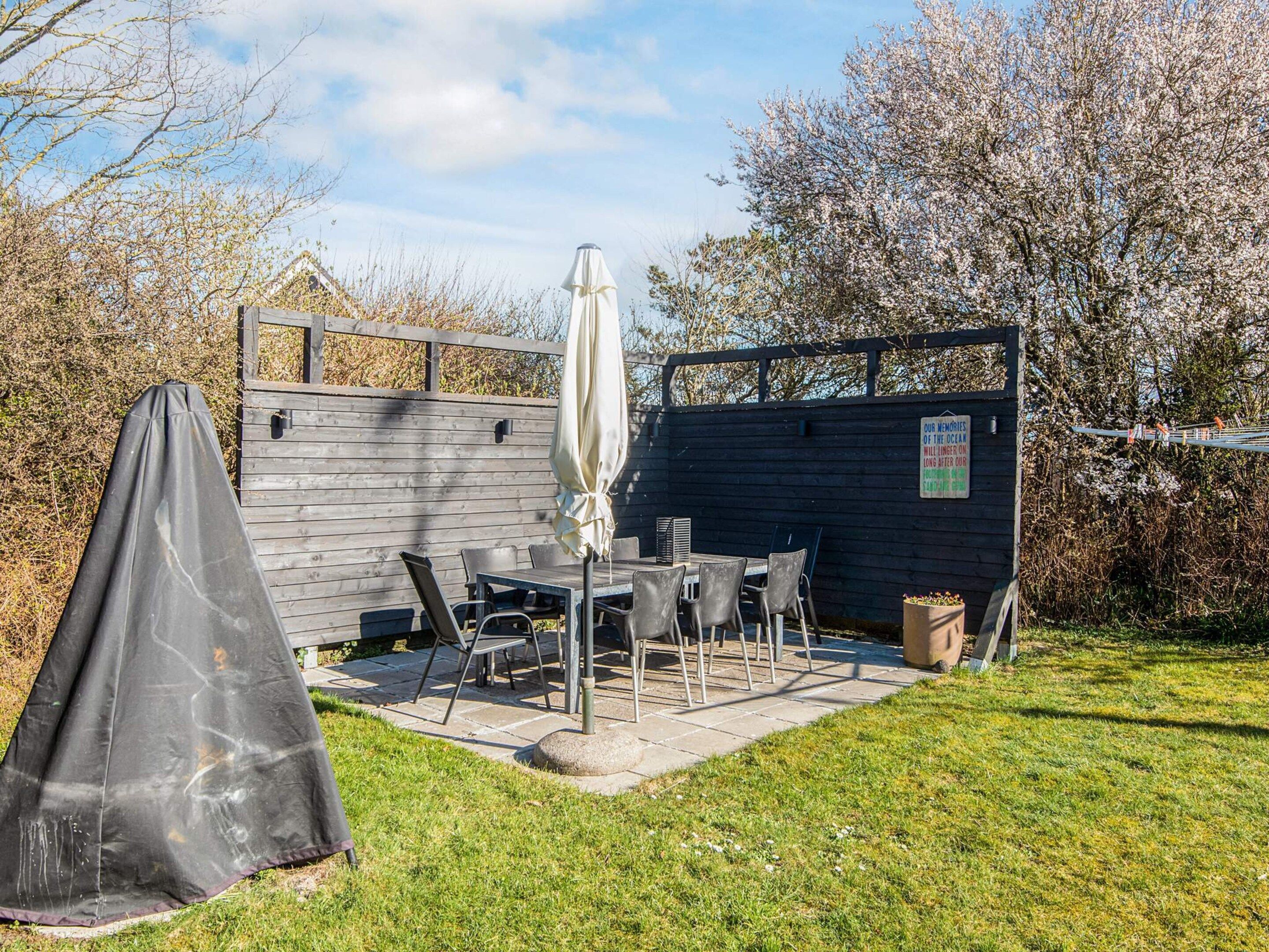Een terras met een tafel en stoelen, een overdekte zithoek en een houten omheining.