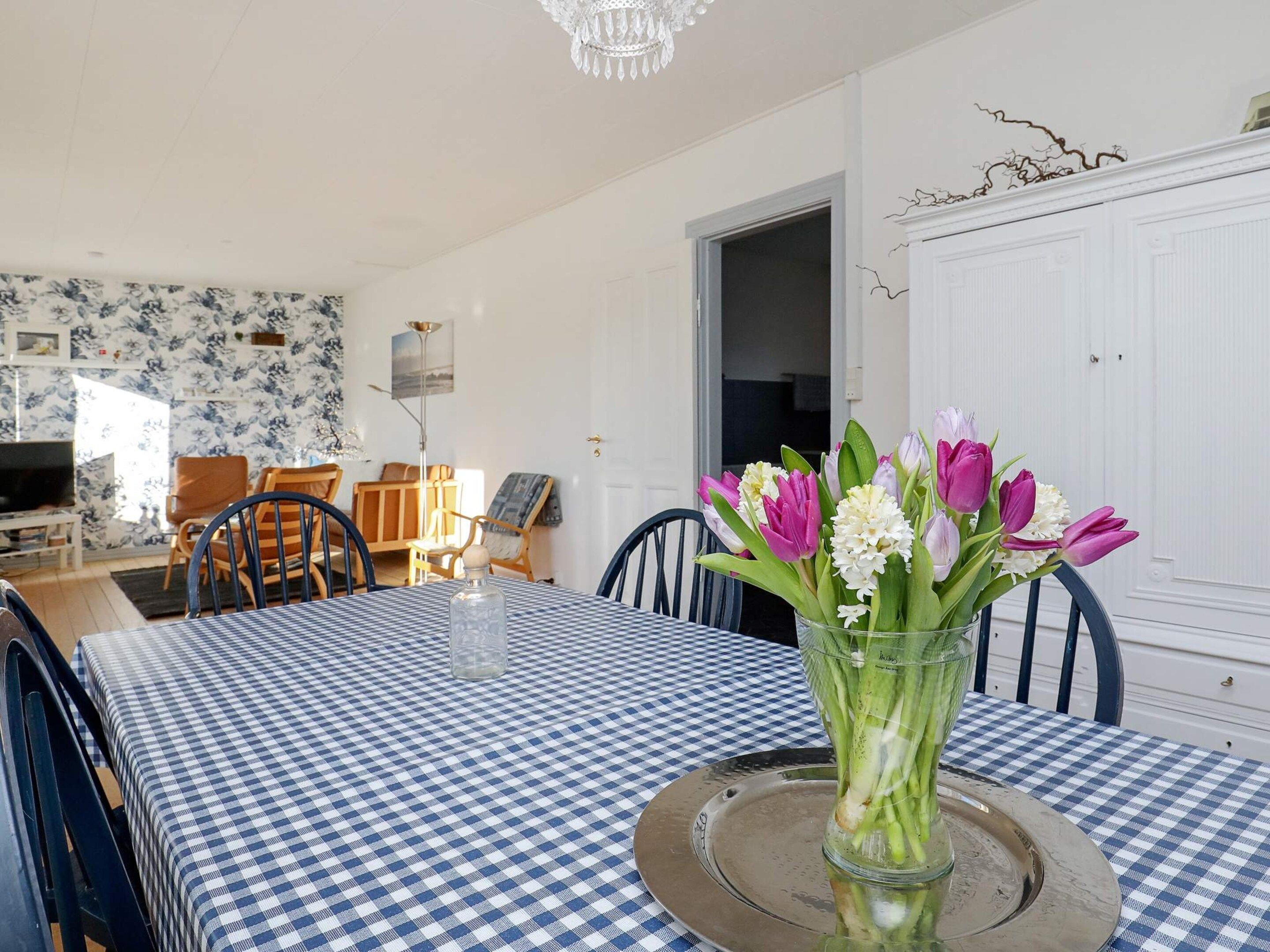 A dining area with a checkered tablecloth, chairs, a vase of flowers, and a chandelier.