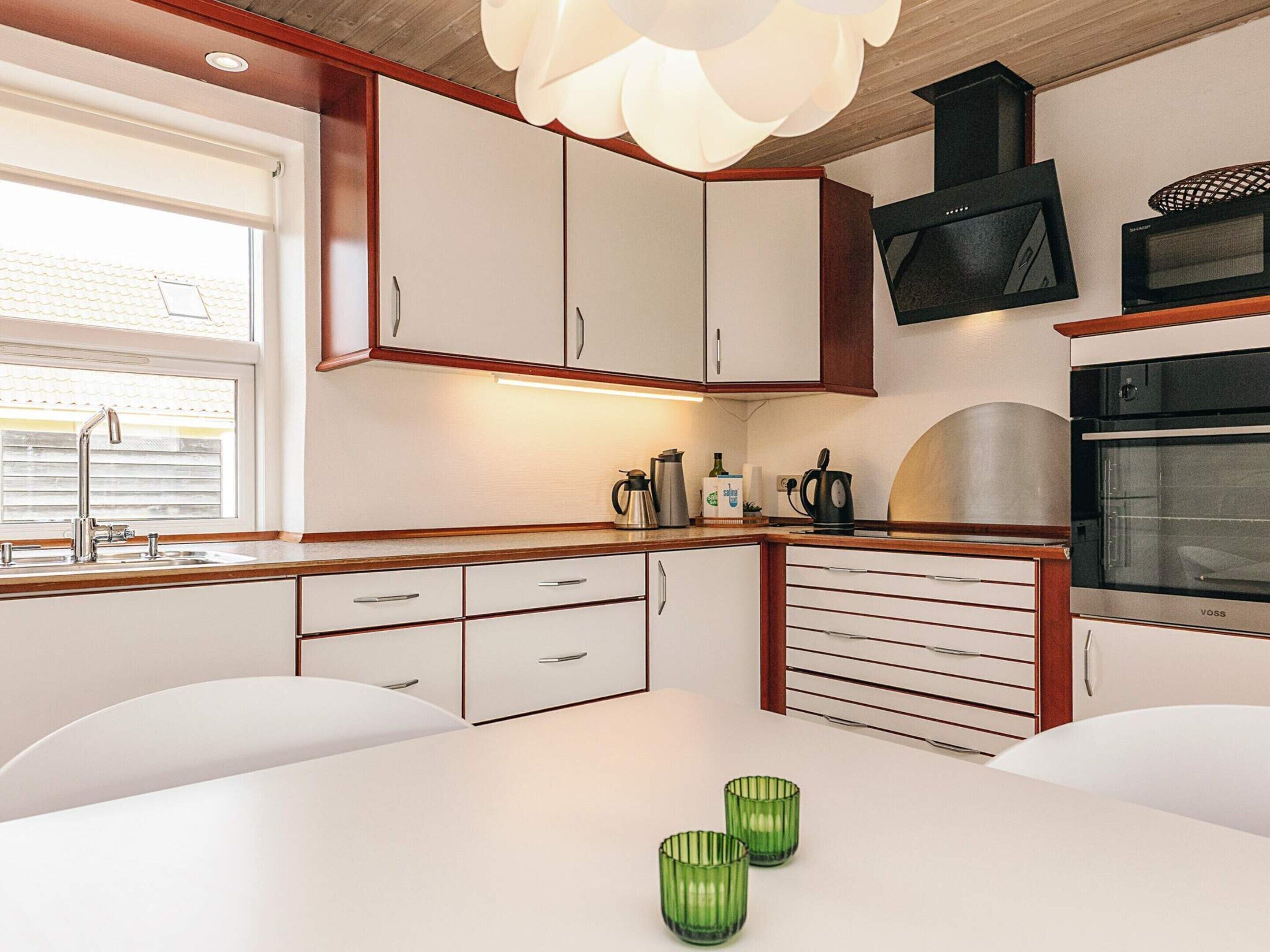 Une cuisine moderne avec des meubles blancs, un évier en acier inoxydable, une bouilloire, une machine à café et un four Voss.