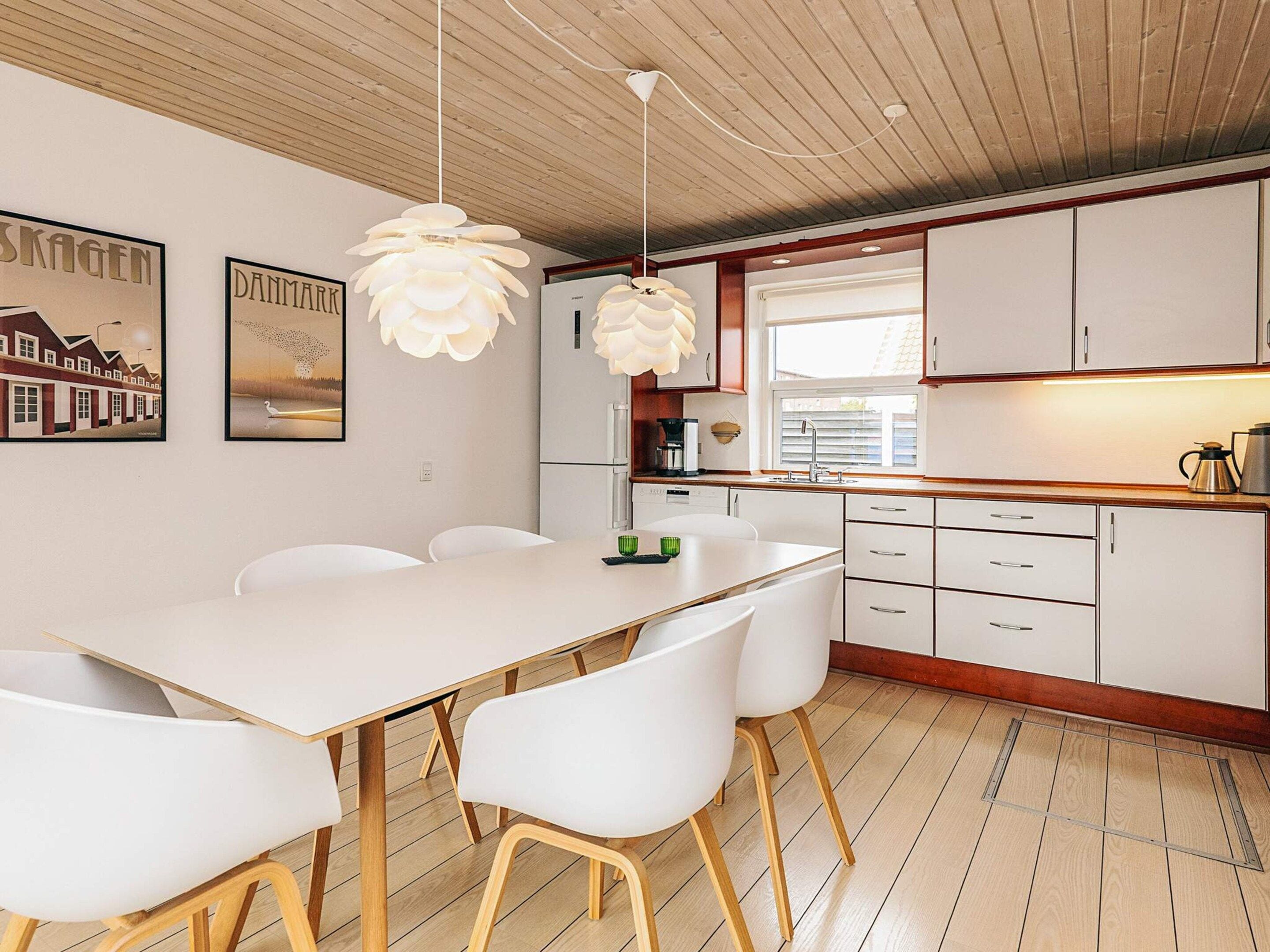 A modern kitchen with white cabinets, a wooden floor, and pendant lights.