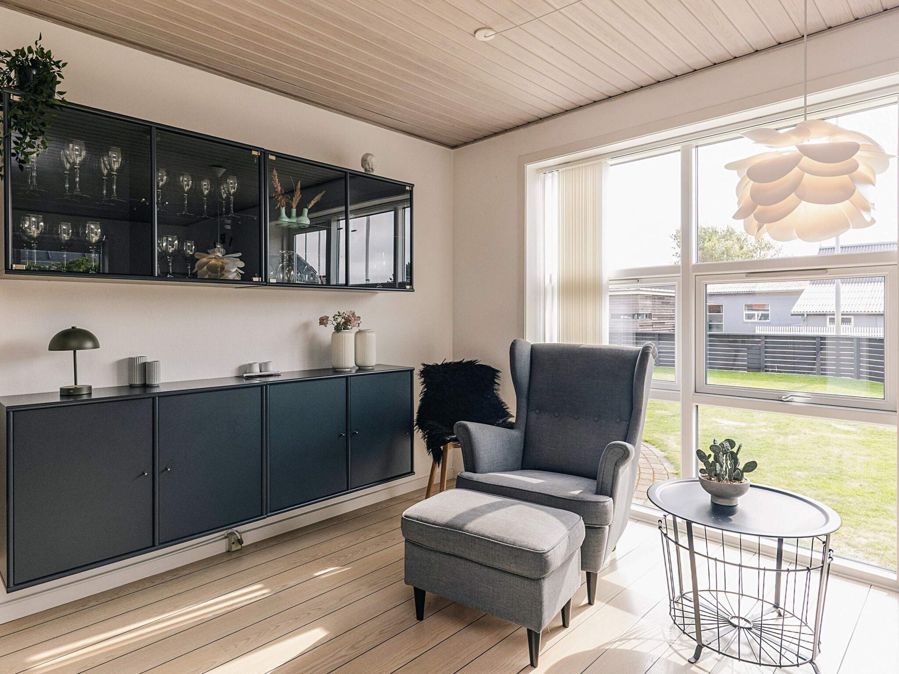 A modern living room with a grey armchair, a small round table, and a cabinet with glassware.