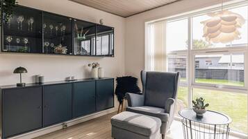 A modern living room with a grey armchair, a small round table, and a cabinet with glassware.