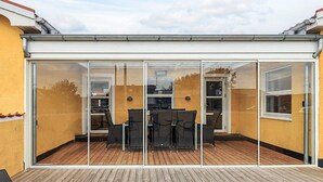 A covered patio with a wooden deck, glass sliding doors, and outdoor furniture.