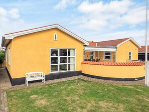 A yellow building with a red roof, a white bench, and a grassy yard.