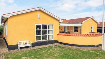A yellow building with a red roof, a white bench, and a small lawn area.