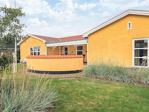 A yellow building with a red-tiled roof, a covered patio, and a grassy yard with tall grasses.