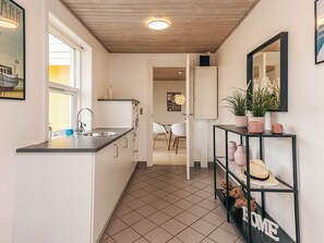 A kitchen with a window, a sink, a countertop, a cabinet, and a door leading to another room.