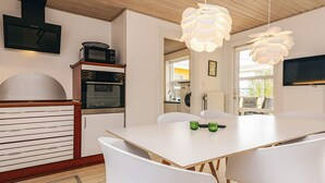 A modern kitchen with a white table and chairs, wooden cabinets, and a hanging light fixture.