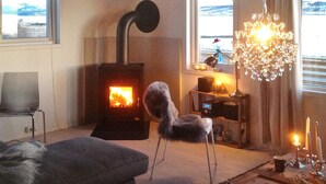 Una habitación acogedora con una estufa de leña, una silla, una mesa con lámpara y un candelabro.