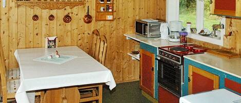 A wooden cabin with a dining area, kitchen, and a window overlooking greenery.