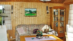 A cozy room with wooden walls, a floral sofa, a wooden coffee table, a bookshelf, and a painting of a landscape. - 3 Person Holiday Home in Frei (Kristiansund)