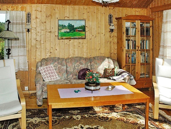 A cozy room with wooden walls, a floral sofa, a wooden coffee table, a bookshelf, and a painting of a landscape. - 3 Person Holiday Home in Frei (Kristiansund)