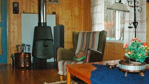 A cozy living room with wooden walls, a fireplace, a chair with a blanket, a table with a bowl, and a window with curtains. - 3 Person Holiday Home in Frei (Kristiansund)