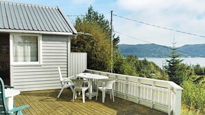 A wooden deck with a white table and chairs, overlooking a lake and mountains. - 3 Person Holiday Home in Frei (Kristiansund)