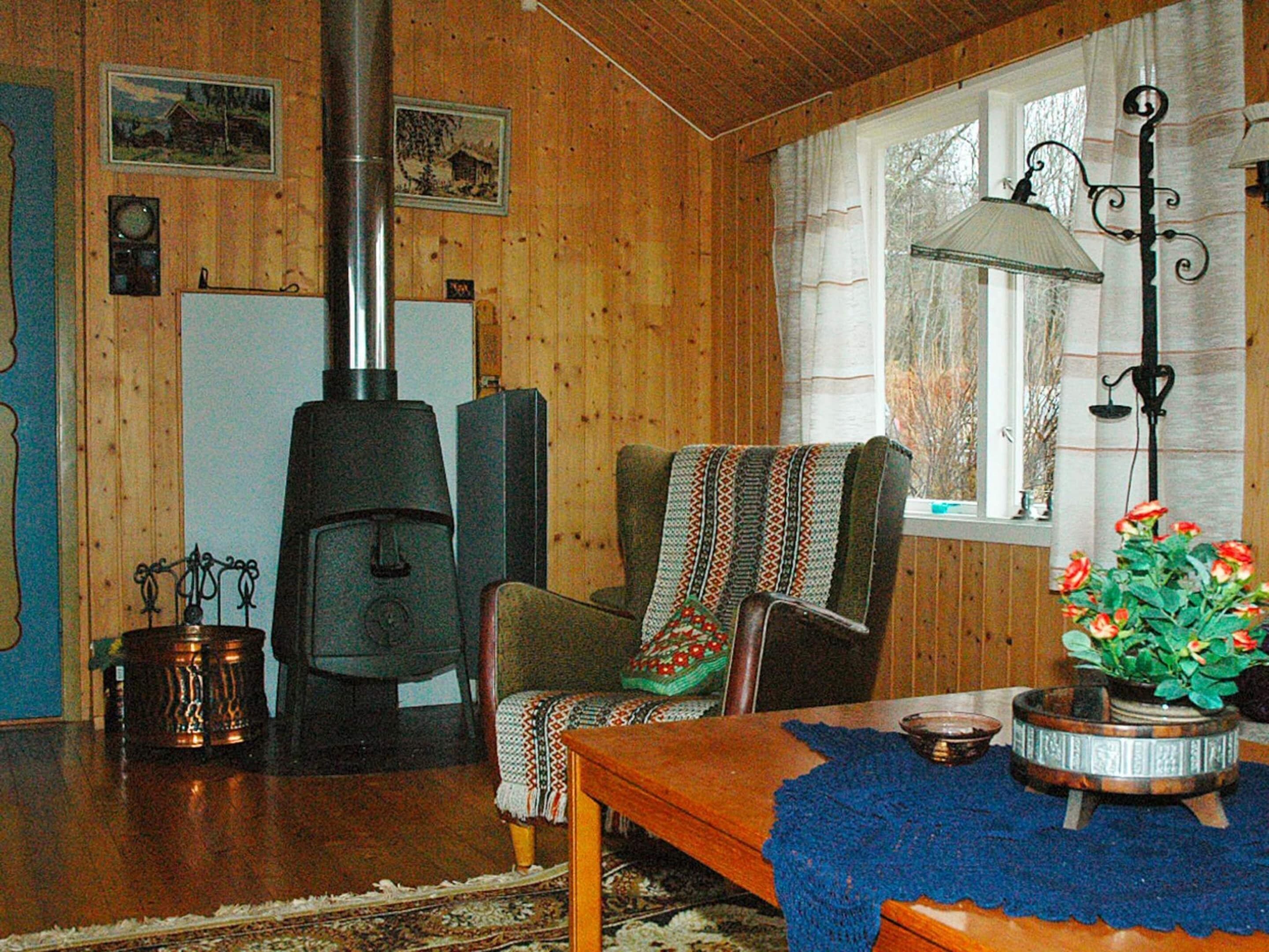 Une pièce chaleureuse avec des murs en bois, une cheminée, un fauteuil avec une couverture, une table avec une plante et une fenêtre avec des rideaux.