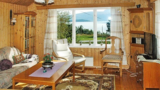 A wooden cabin interior with a sofa, two chairs, a table, a TV, and a view of a lake through a window. - 3 Person Holiday Home in Frei (Kristiansund)