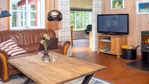 Ein gemütliches Wohnzimmer mit Ledersofa, Couchtisch aus Holz und einem Fernseher auf einem Holzständer.