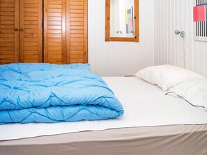 A bedroom with a bed, a wooden wardrobe, and a window with blinds.