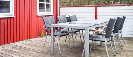 A red building with a white window and a deck with a table and chairs.