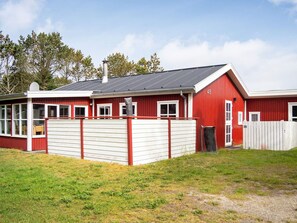 A red and white building with a covered porch, a fenced yard, and a grassy area.