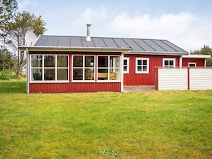 A red house with a large windowed front section, a chimney, and a fenced yard.
