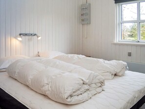 A room with two beds, a wall-mounted light fixture, and a window with a view of trees.