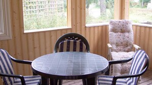 A covered patio with a round table and four striped chairs, large windows, and a wooden fence in the background. - 5 Person Holiday Home in Mellbystrand (Mellbystrand)