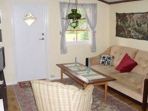 A living room with a beige sofa, a patterned armchair, a wooden coffee table with candles, and a green hanging lamp. - 5 Person Holiday Home in Mellbystrand (Mellbystrand)
