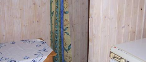 A room with a wooden wall, a table with a patterned tablecloth, a curtain with floral design, and a washing machine.