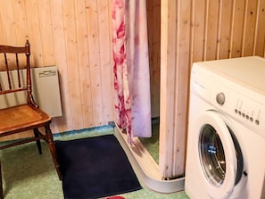 A laundry area with a washing machine, a chair, and a shower curtain.