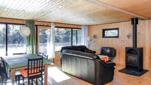 A cozy living room with a wooden floor, a sofa, a dining table with chairs, a television, and a wood-burning stove.